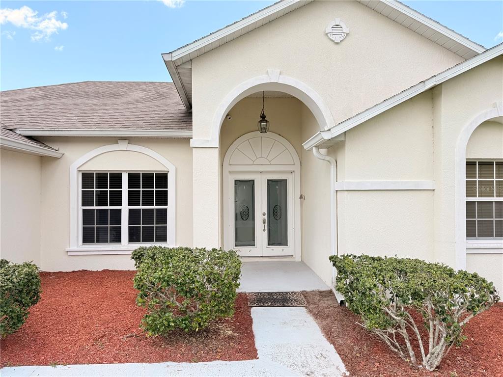 The exterior of a house features a beige stucco facade, double front doors, and landscaping — 3010 VICTORIA DRIVE, KISSIMMEE, FL