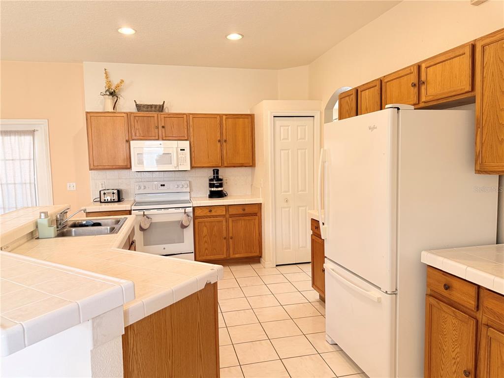 A kitchen features oak cabinets, white appliances, tiled countertops, and a white tile floor — 3010 VICTORIA DRIVE, KISSIMMEE, FL