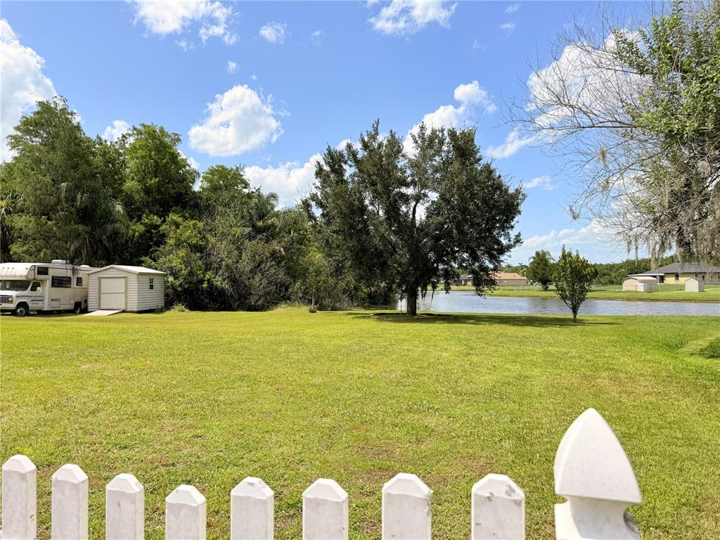 A grassy backyard features a white picket fence, a shed, a camper, and a pond — 3010 VICTORIA DRIVE, KISSIMMEE, FL