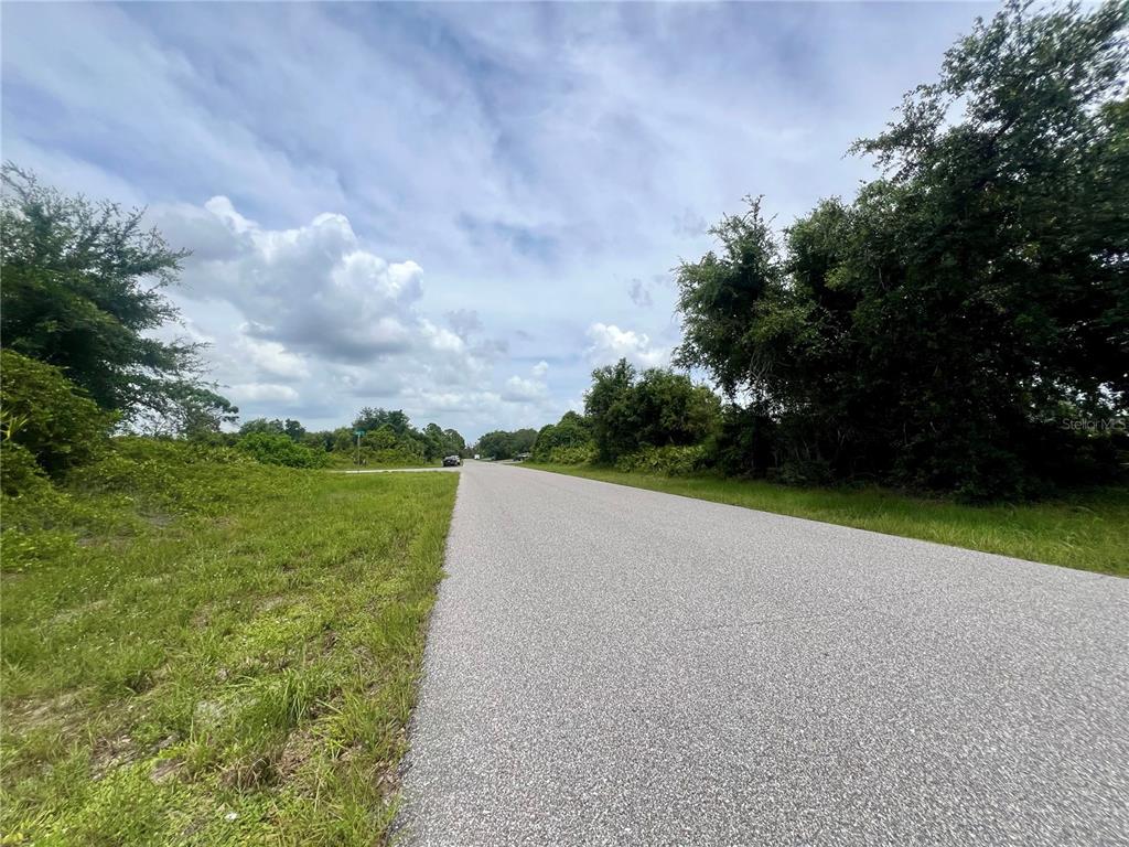 A paved road stretches through a rural area with grassy shoulders and dense trees — 12322 ALBRECHT TERRACE, PORT CHARLOTTE, FL
