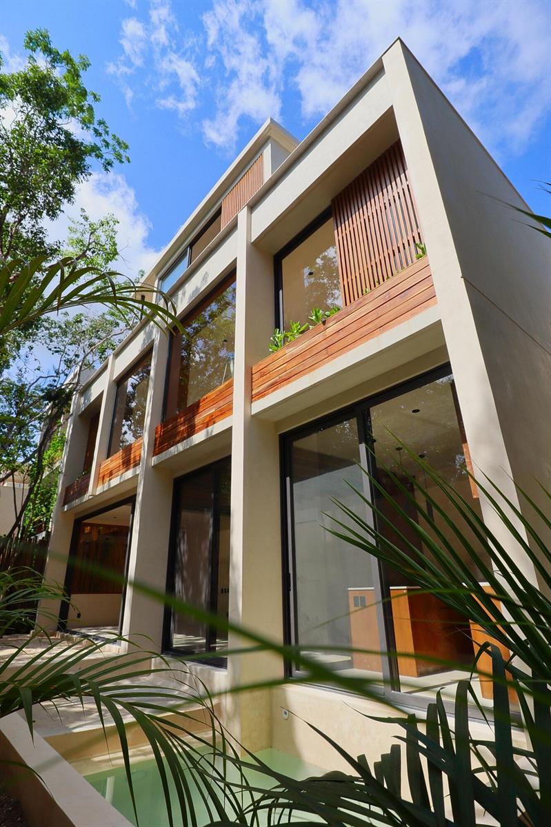 A modern three-story house exterior features large glass windows, wood slat accents, and a pool — Amari Tulum 10 Avenida Norte & Calle Palma Unit 16h, FL