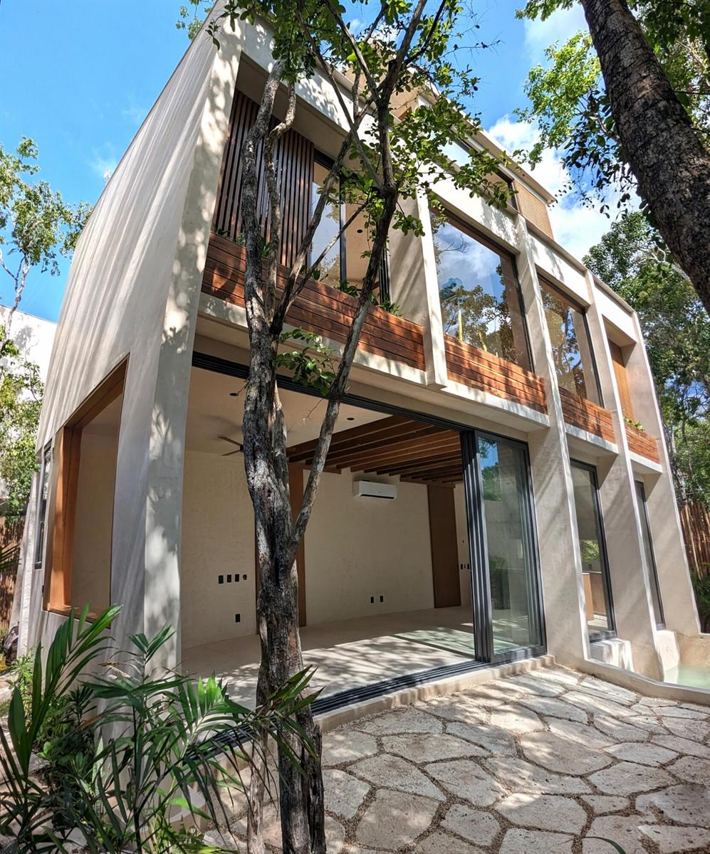 A modern two-story house features large glass sliding doors opening to a stone patio — Amari Tulum 10 Avenida Norte & Calle Palma Unit 16h, FL