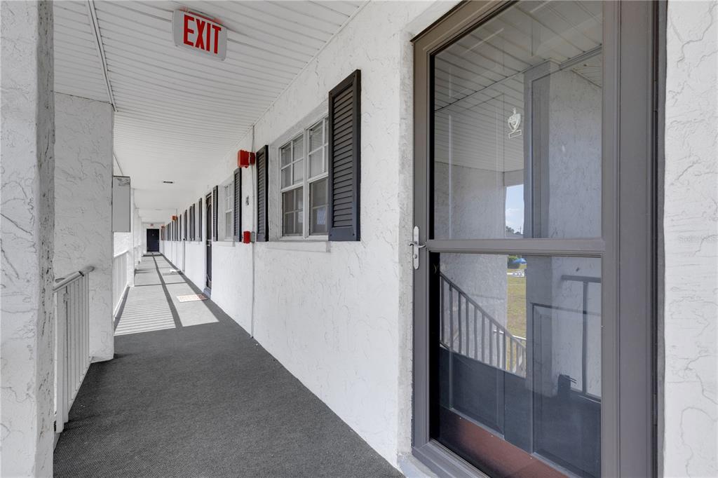 An exterior walkway with a grey carpeted floor, white stucco walls, and several apartment doors — 105 47TH AVENUE DRIVE W UNIT 376, BRADENTON, FL