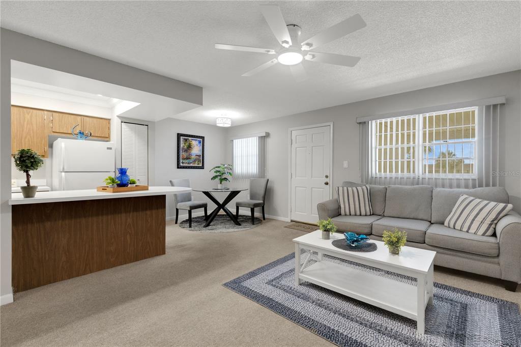 An open-concept living and dining area features a kitchen island, gray sofa, and ceiling fan — 105 47TH AVENUE DRIVE W UNIT 376, BRADENTON, FL