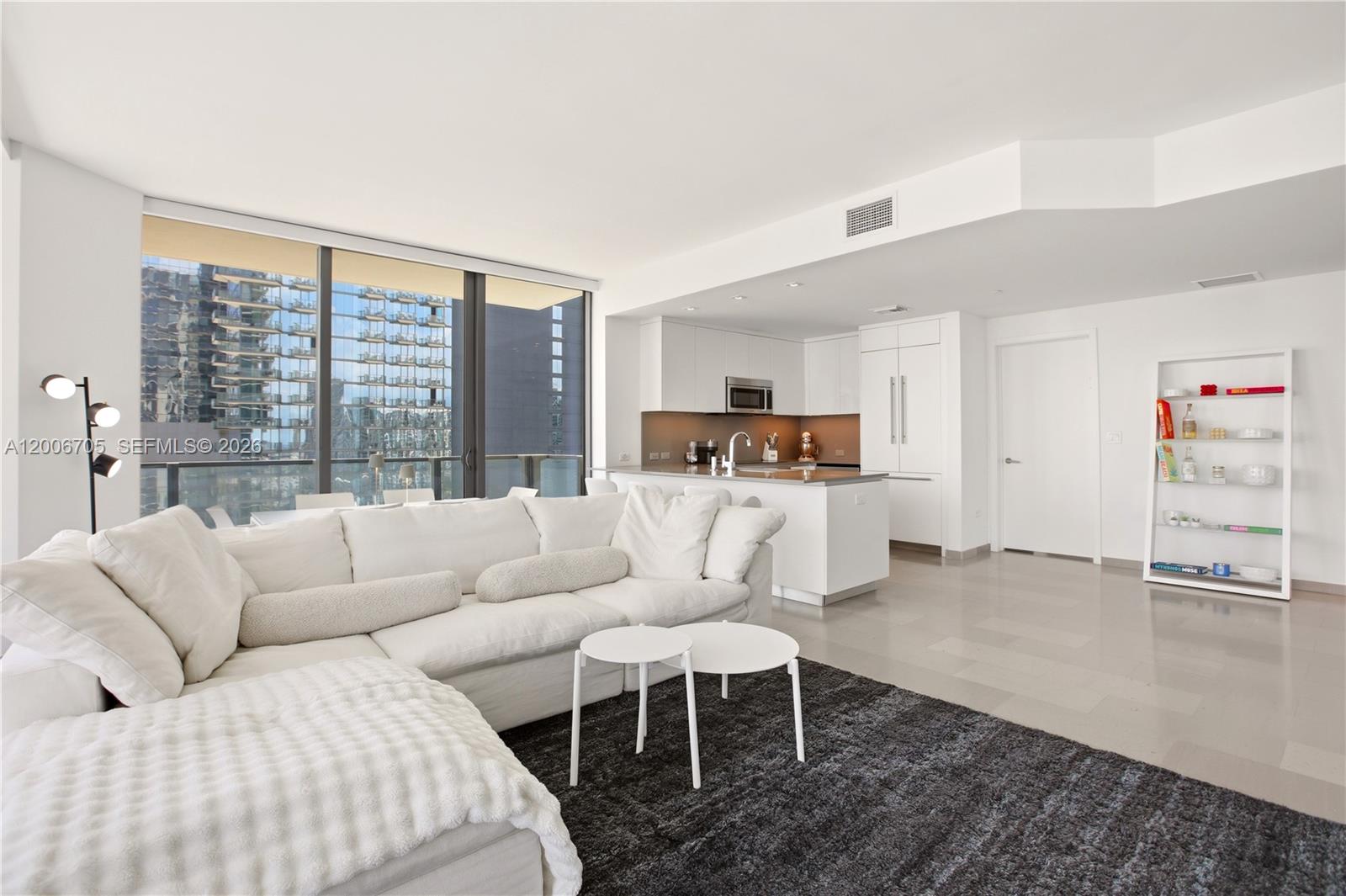 A modern living room features a white sectional sofa, a dark rug, and an open kitchen — 68 SE 6th St # 2701, Miami FL 33131, MIAMI, FL