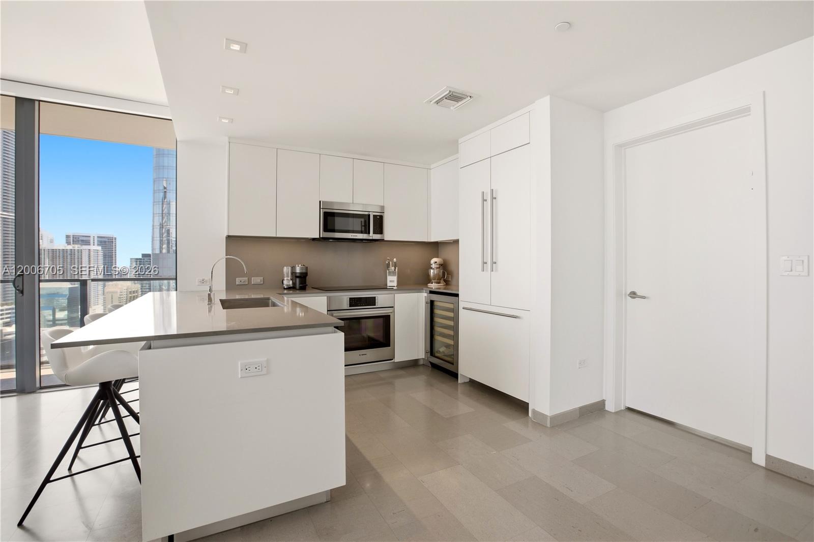 A modern kitchen features white cabinetry, stainless steel appliances, a center island, and floor-to-ceiling windows — 68 SE 6th St # 2701, Miami FL 33131, MIAMI, FL