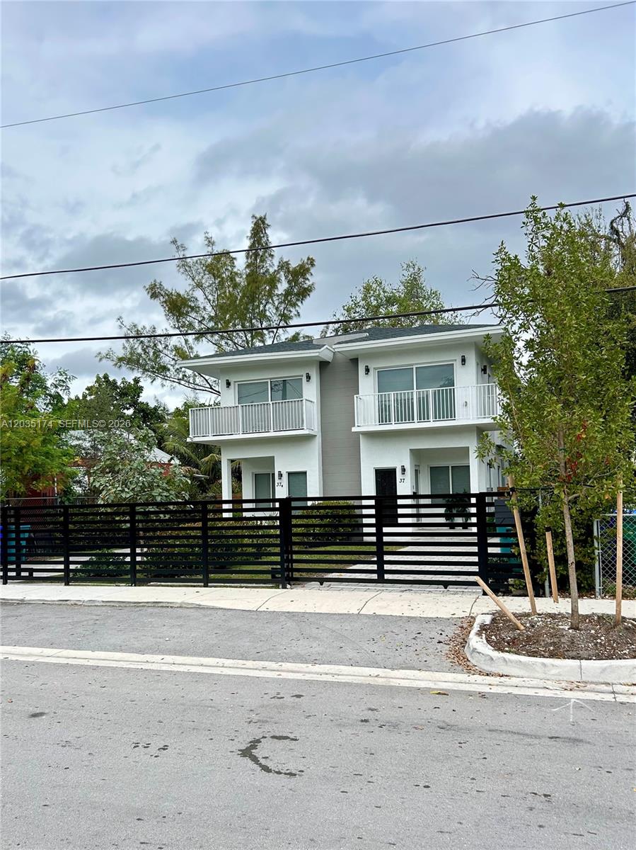 A two-story duplex with white siding, balconies, and a black metal fence in front — 37 NW 70th St, Miami FL 33150, MIAMI, FL