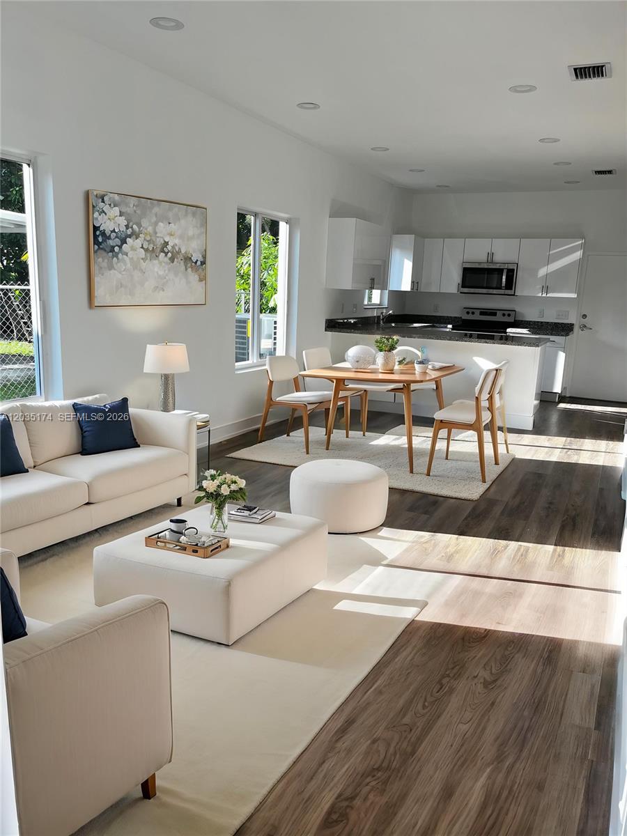 An open-concept living and dining area features white furniture, wood flooring, and a modern kitchen — 37 NW 70th St, Miami FL 33150, MIAMI, FL
