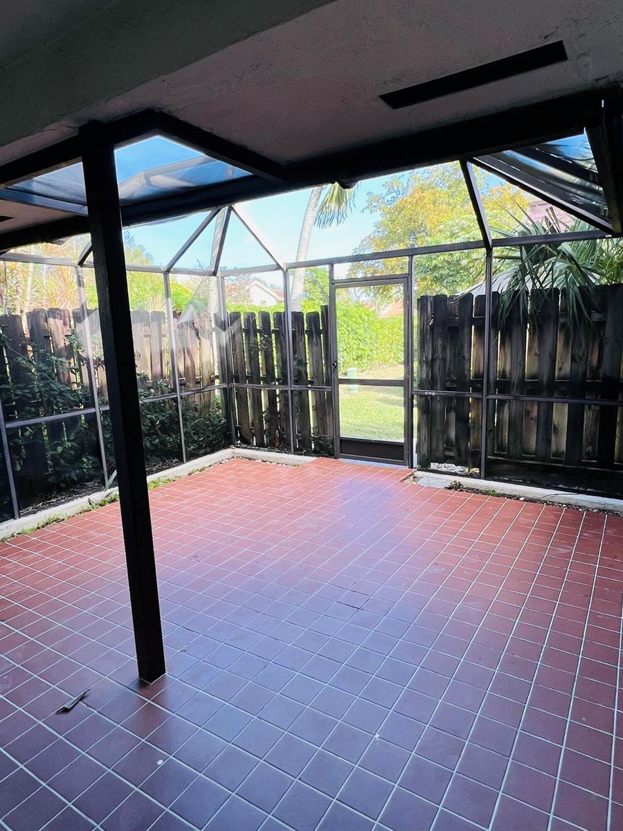 A screened-in patio with red tile flooring, a black metal frame, and a wooden fence — 7482 E Courtyard Run E, Boca Raton FL 33433, BOCA RATON, FL