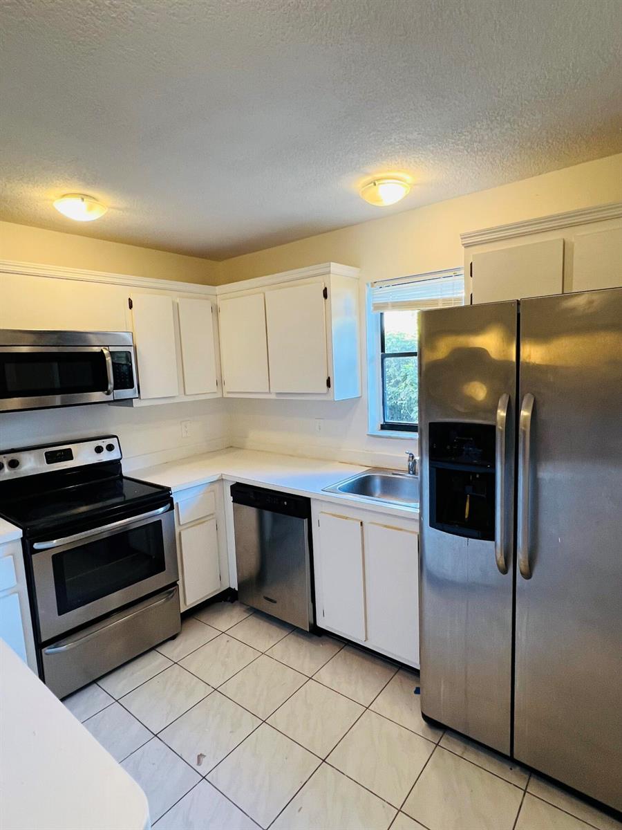 A kitchen features white cabinets, stainless steel appliances, white countertops, and light-colored tile flooring — 7482 E Courtyard Run E, Boca Raton FL 33433, BOCA RATON, FL