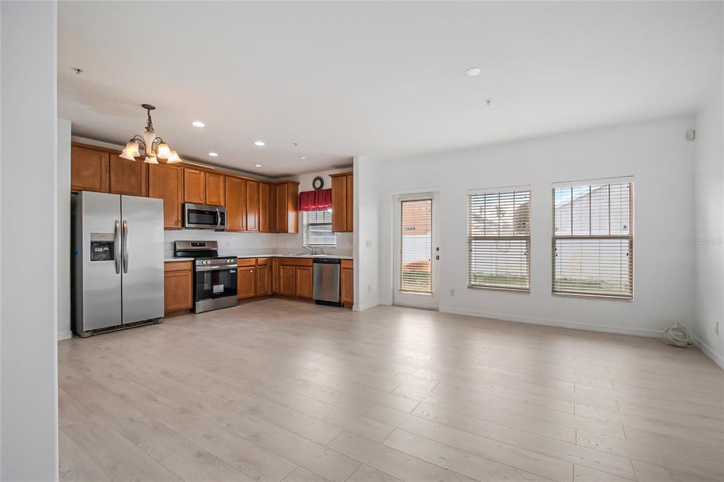 An open-concept kitchen and living area featuring light wood-look flooring and stainless steel appliances — 2018 CYPRESS BAY BOULEVARD, KISSIMMEE, FL