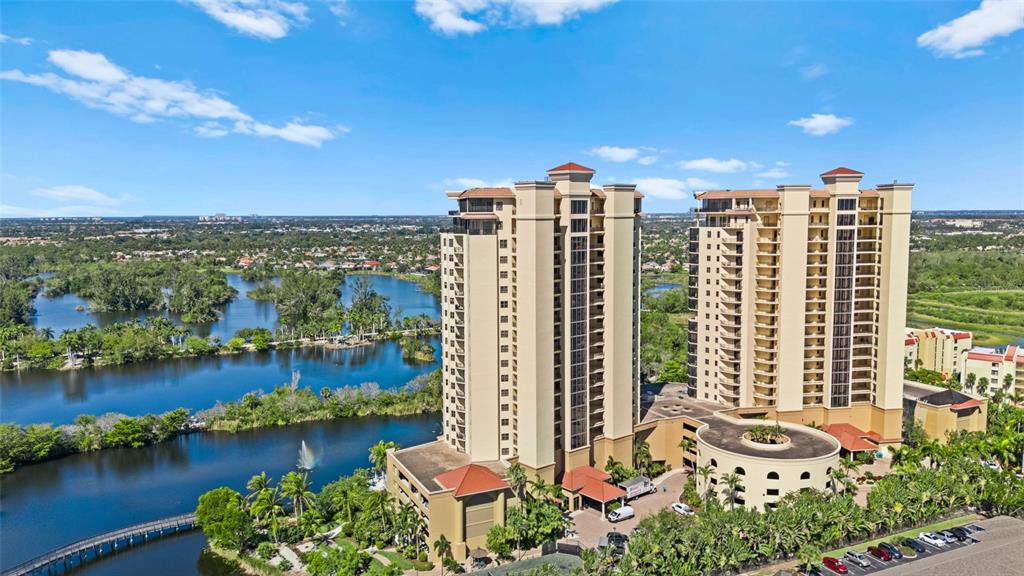 An aerial view of two tall residential towers surrounded by a lake and lush greenery — 14380 RIVA DEL LAGO DRIVE UNIT 1804, FORT MYERS, FL