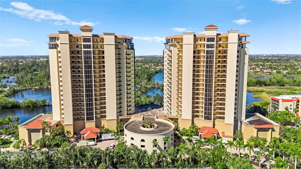 An aerial view shows two tall, beige residential towers connected by a circular base structure — 14380 RIVA DEL LAGO DRIVE UNIT 1804, FORT MYERS, FL