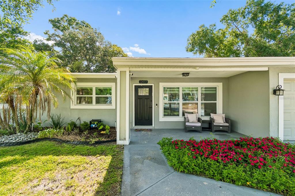 A covered porch features two wicker chairs and a garden bed with pink flowers — 12417 N ROME AVENUE, TAMPA, FL