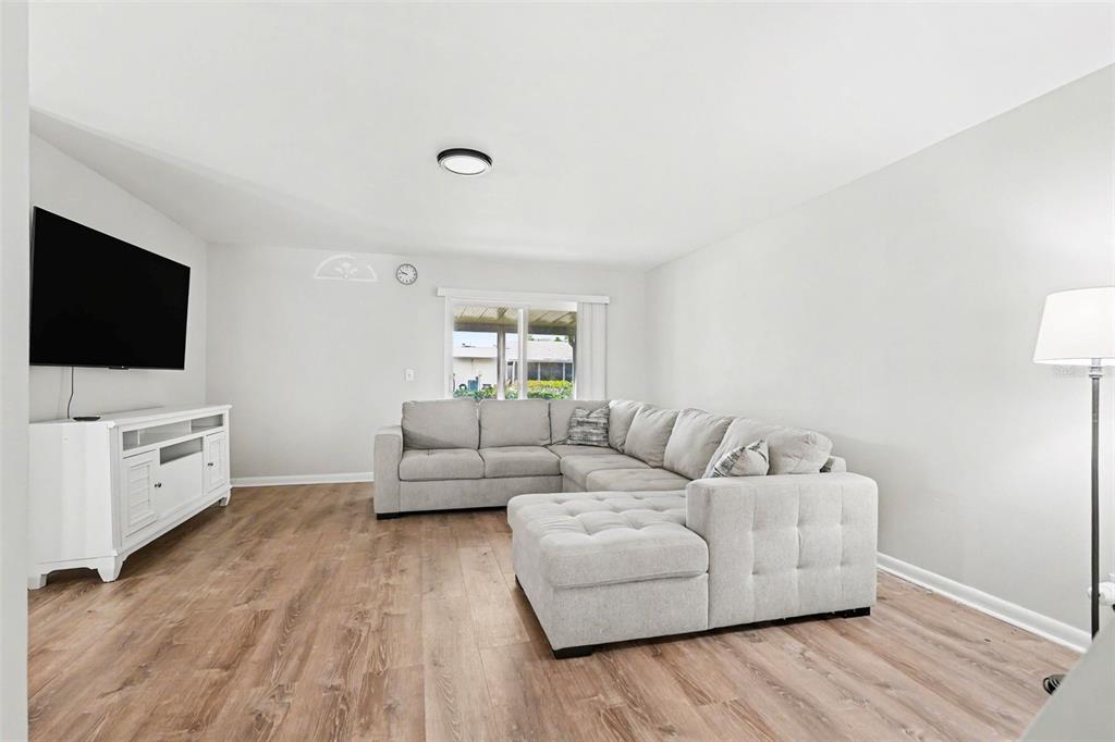 A living room features light wood-look flooring, a white media console, and a gray sectional — 3267 39TH STREET S UNIT B, ST PETERSBURG, FL