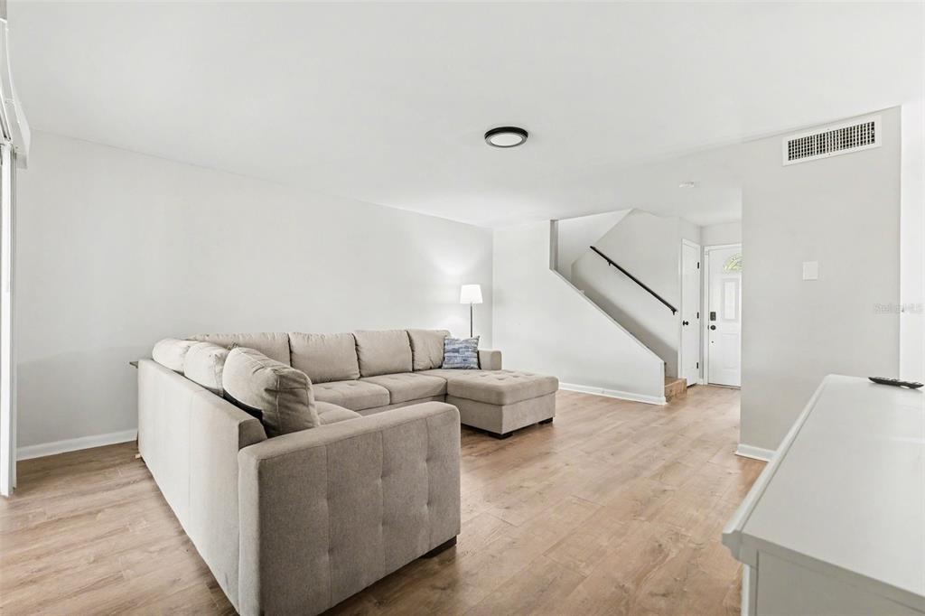 A living room features a large sectional sofa, light wood flooring, and stairs to the upper level — 3267 39TH STREET S UNIT B, ST PETERSBURG, FL