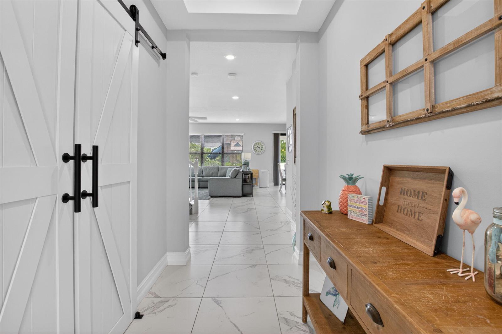 A hallway with white marble-look tile floors leads to a living room with sliding doors — 8787 Grand Prix Lane, Boynton Beach FL 33472, BOYNTON BEACH, FL