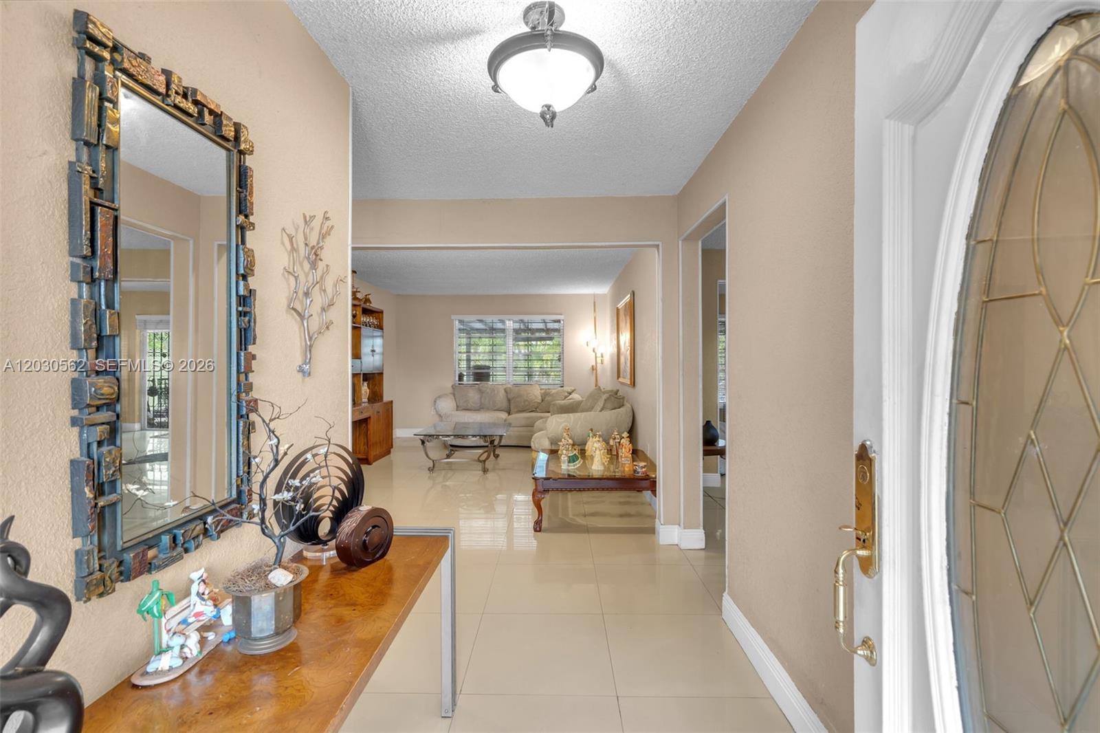 An entryway with a decorative mirror and console table leads into a tiled living room — 1320 SW 84th Ave, Miami FL 33144, MIAMI, FL