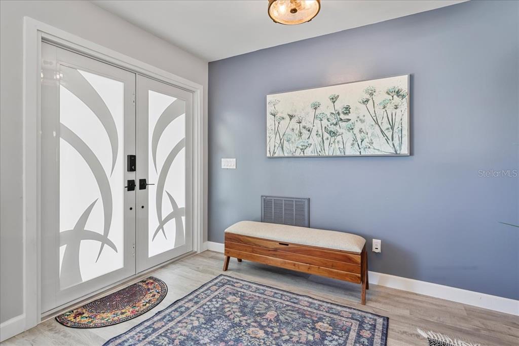 An entryway features a double glass door, a wooden storage bench, and a blue wall — 206 SE 45TH TERRACE, CAPE CORAL, FL
