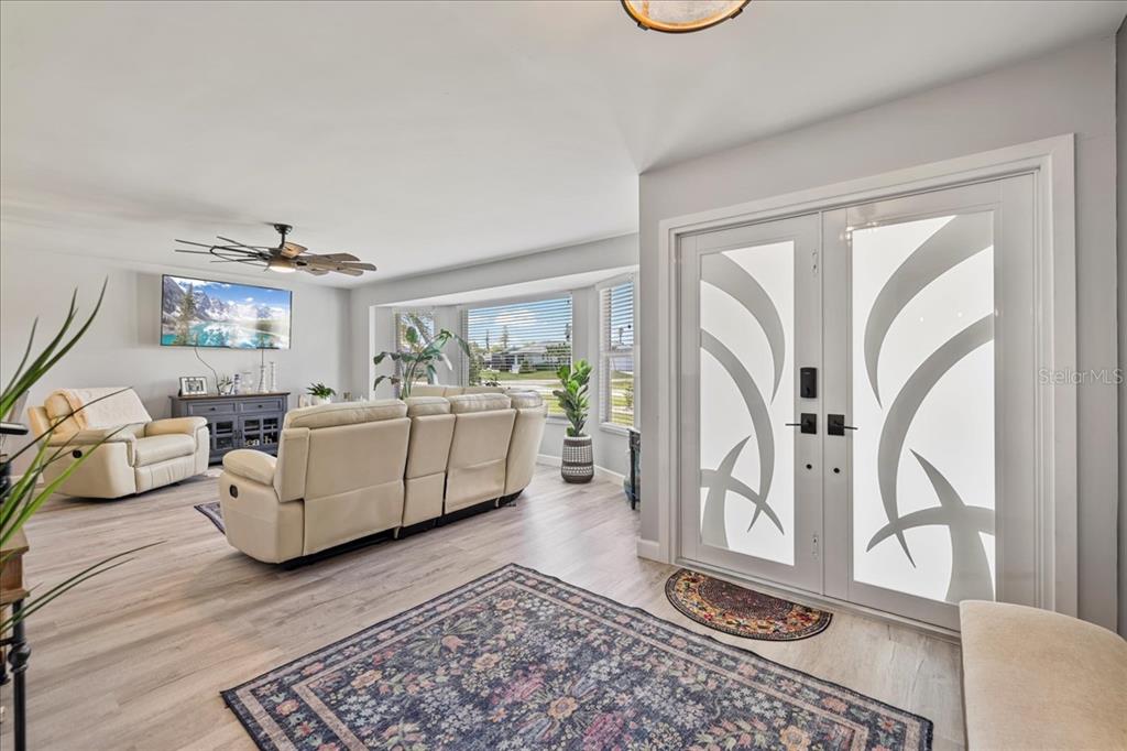 A living room features light wood flooring, a cream sectional, and double glass-paneled entry doors — 206 SE 45TH TERRACE, CAPE CORAL, FL