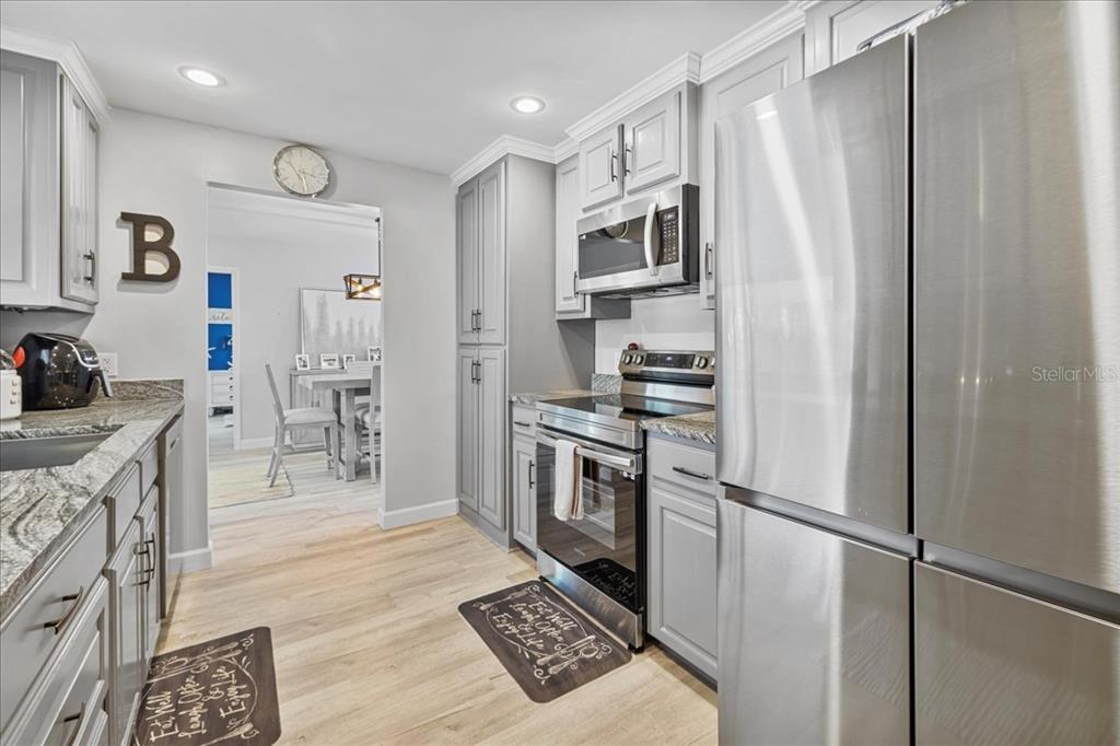 A kitchen features gray cabinets, stainless steel appliances, granite countertops, and light wood flooring — 206 SE 45TH TERRACE, CAPE CORAL, FL