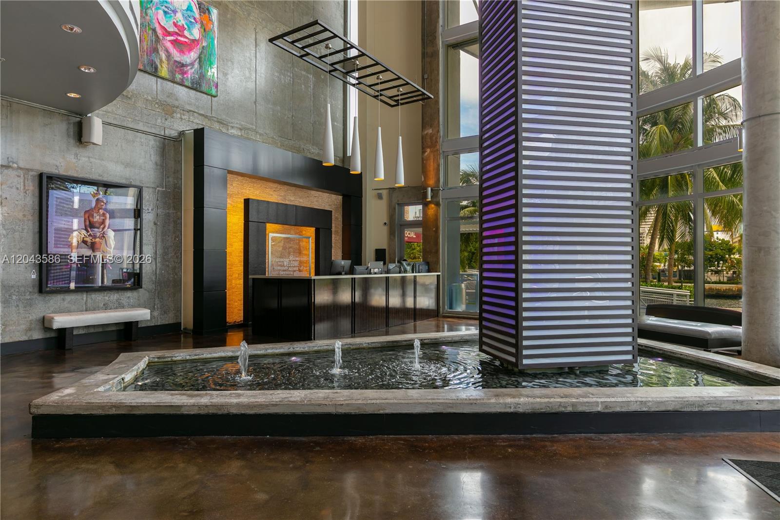 A modern building lobby features a reception desk, a central water fountain, and concrete walls — 690 SW 1st Ct, Miami FL 33130, MIAMI, FL