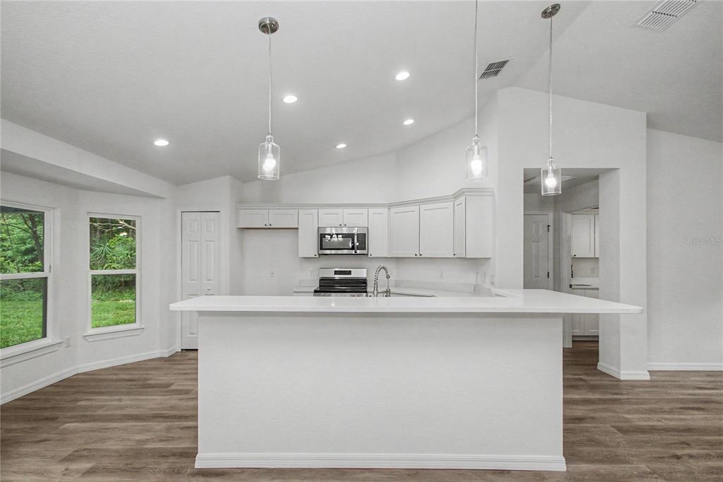 A kitchen features white cabinets, stainless steel appliances, a breakfast bar, and wood-look flooring — 3032 SE 140TH PLACE, SUMMERFIELD, FL