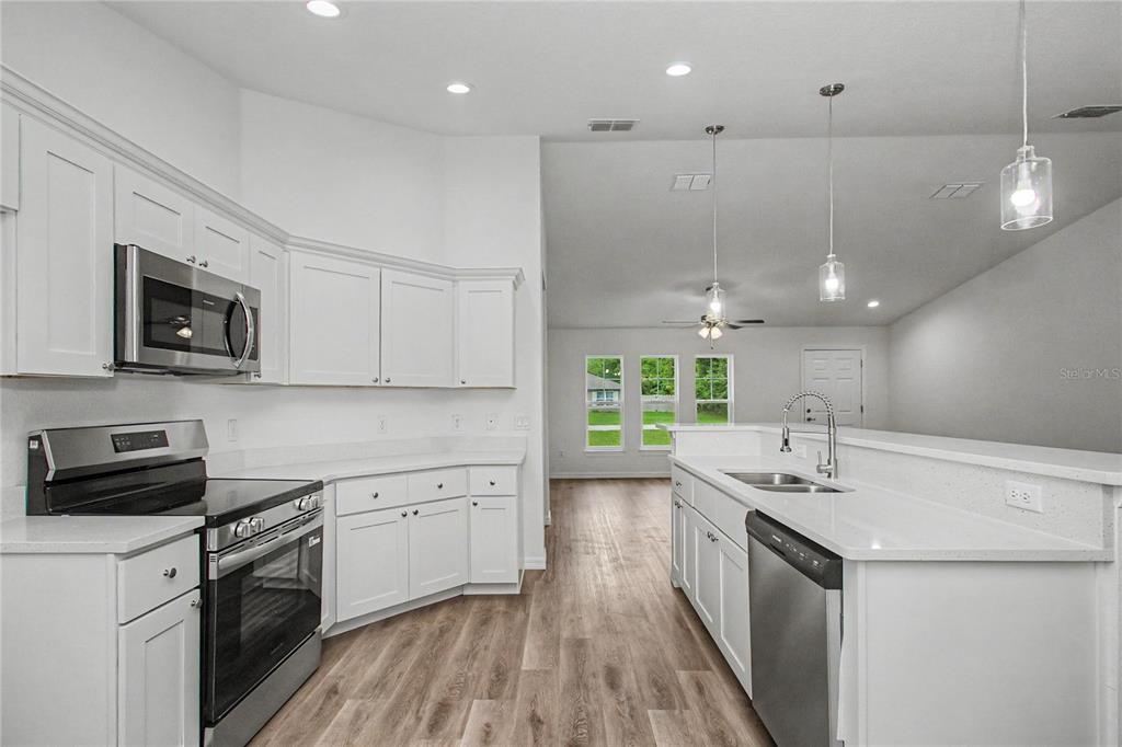 A modern kitchen features white cabinets, stainless steel appliances, and light wood-look flooring — 3032 SE 140TH PLACE, SUMMERFIELD, FL