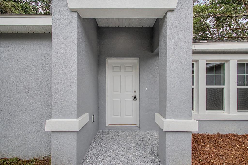 A white front door is recessed between two gray stucco pillars on a concrete porch — 3032 SE 140TH PLACE, SUMMERFIELD, FL