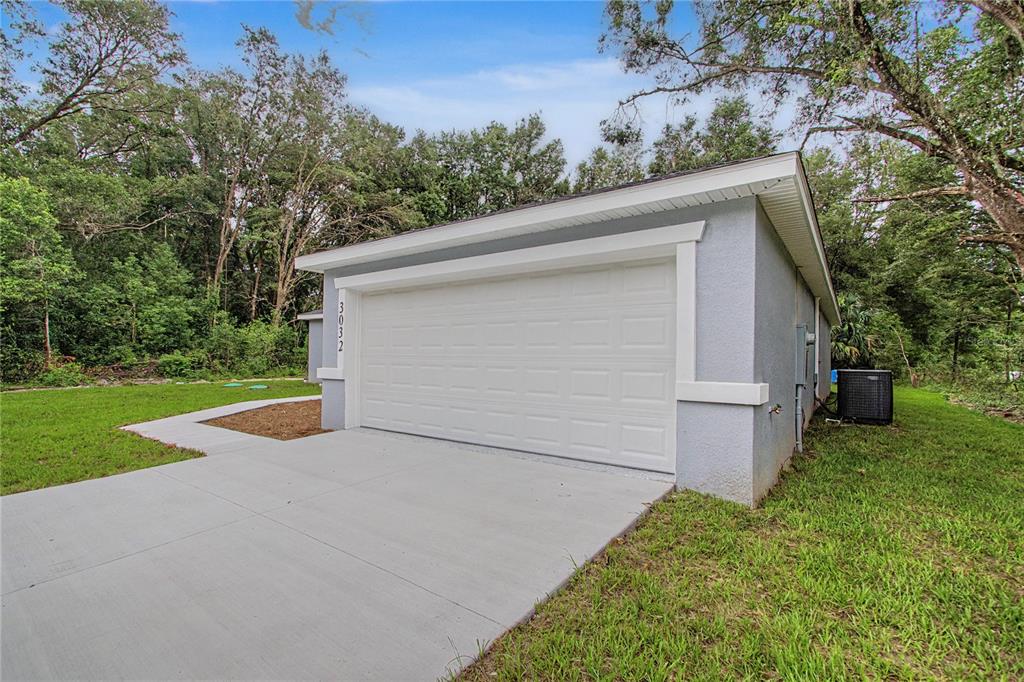 A detached garage with a white door and light gray stucco siding sits on grass — 3032 SE 140TH PLACE, SUMMERFIELD, FL