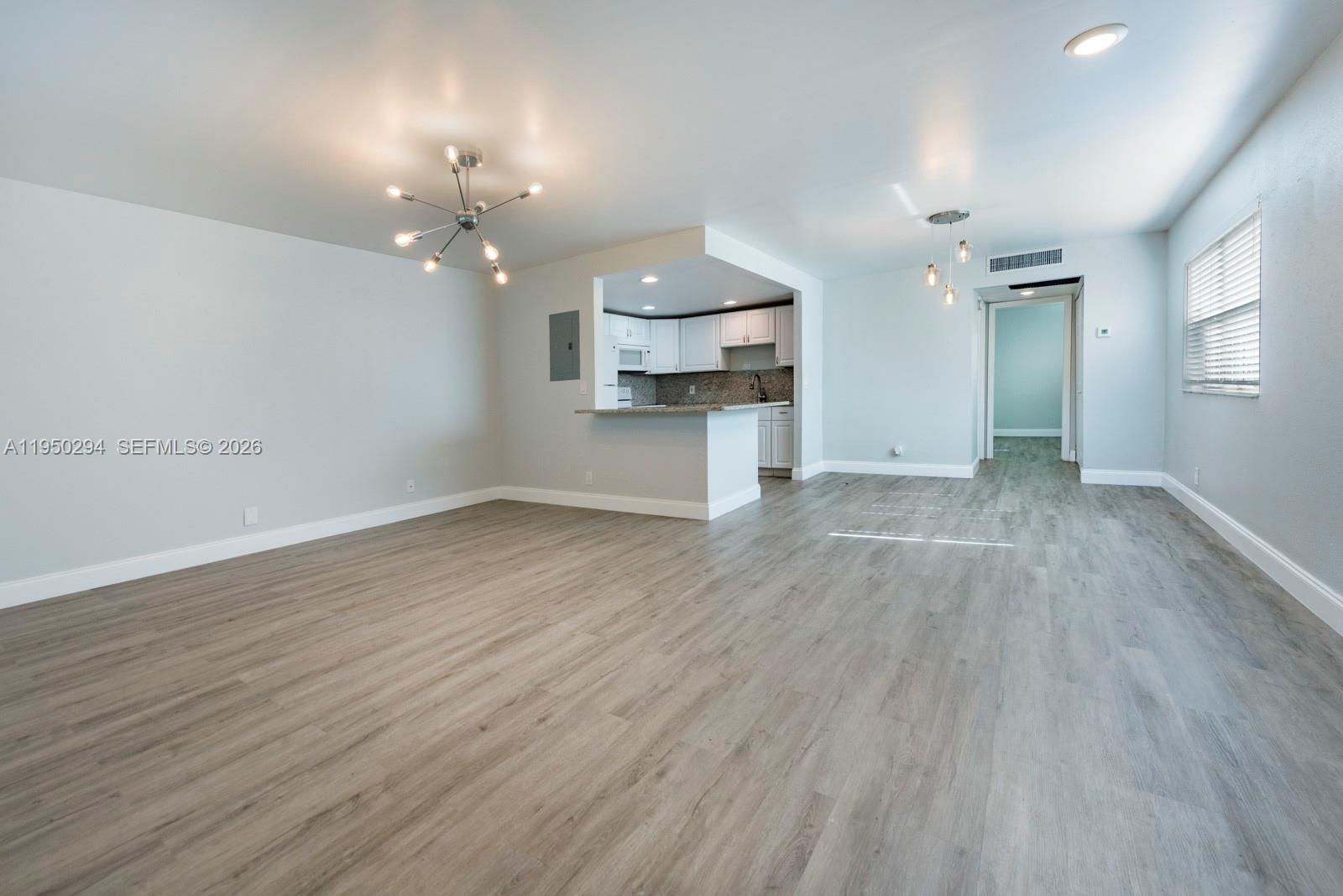 An open-concept living area features light gray walls, wood-look flooring, and a pass-through kitchen — 494 Monaco K # 494, Delray Beach FL 33446, DELRAY BEACH, FL