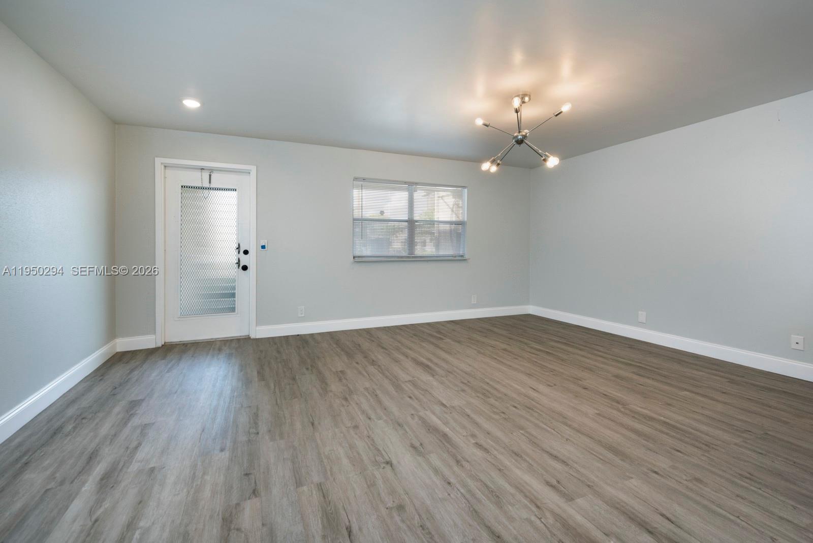 An empty room features light gray walls, wood-look flooring, a window with blinds, and a chandelier — 494 Monaco K # 494, Delray Beach FL 33446, DELRAY BEACH, FL