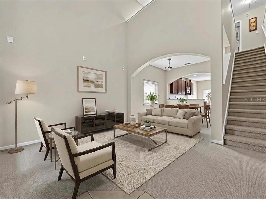 A living room with high ceilings, a staircase, and an arched opening to the dining area — 10411 PARK COMMONS DRIVE, ORLANDO, FL
