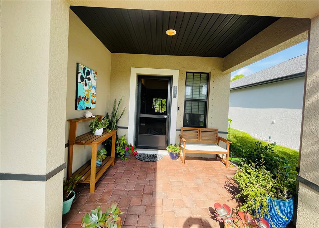A covered front porch features a brick floor, a wooden bench, and potted plants — 15321 MILLE FIORE BOULEVARD, PORT CHARLOTTE, FL
