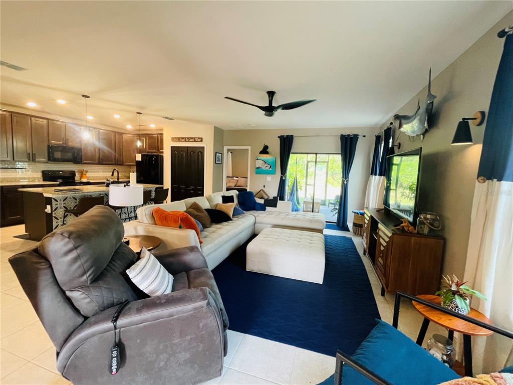 A living room with a sectional sofa, dark blue rug, and an open-concept kitchen — 15321 MILLE FIORE BOULEVARD, PORT CHARLOTTE, FL