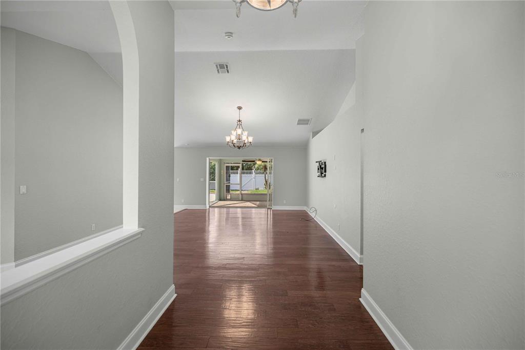 A view through a hallway into a living area with wood floors and a chandelier — 5898 SW 89TH PLACE, OCALA, FL