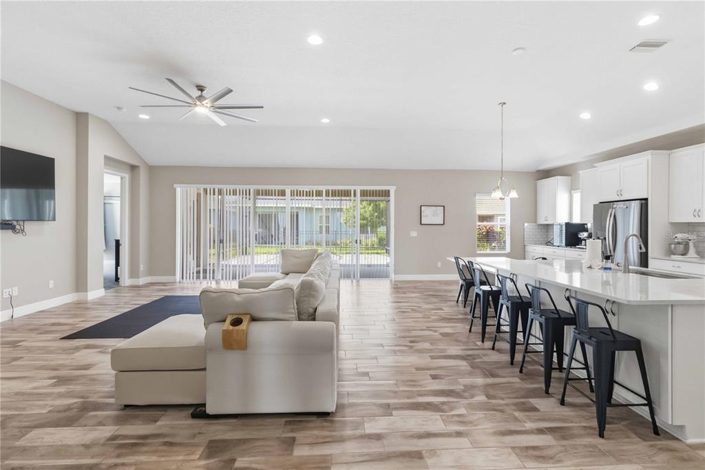 An open-concept living room and kitchen featuring light wood-look tile floors and white cabinetry — 7526 PARADISO DRIVE, APOLLO BEACH, FL