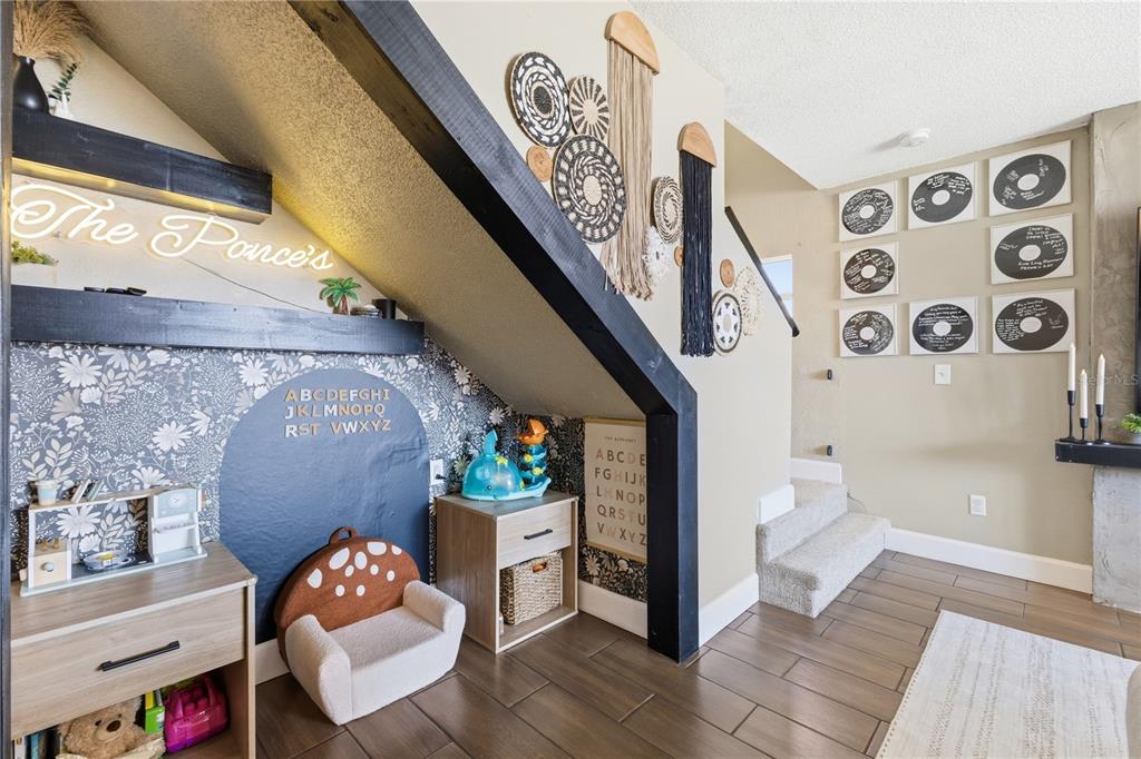 A child's play area is tucked under a staircase with floral wallpaper and wooden shelving — 805 BELVOIR DRIVE, DAVENPORT, FL