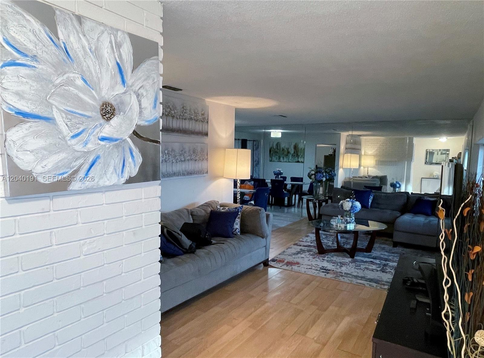 A living room features a white brick wall, gray sectional sofas, and a glass coffee table — 8330 NW 20th Ct, Sunrise FL 33322, SUNRISE, FL