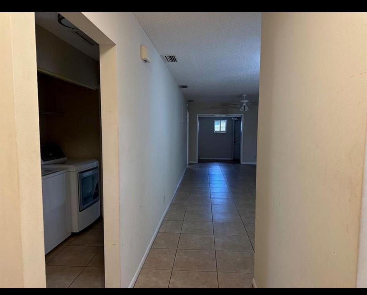 A view down a tiled hallway toward a windowed room with a laundry closet nearby — 8682 Satalite Terrace, West Palm Beach FL 33403, WEST PALM BEACH, FL