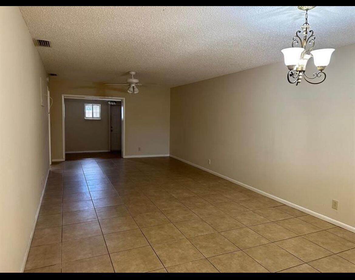 An empty room with tan tile flooring, beige walls, a ceiling fan, and a chandelier — 8682 Satalite Terrace, West Palm Beach FL 33403, WEST PALM BEACH, FL