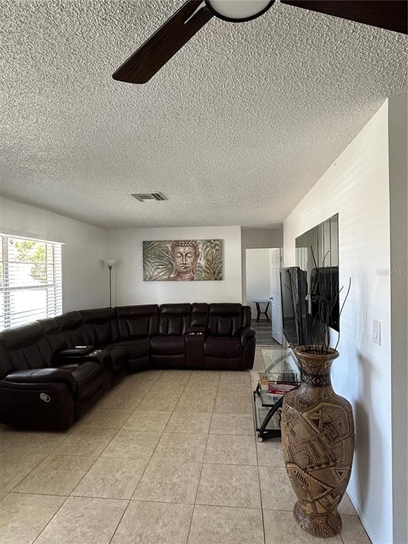 A living room features a large brown sectional sofa, tiled floors, and a decorative floor vase — 7808 OSTEEN ROAD, NEW PORT RICHEY, FL