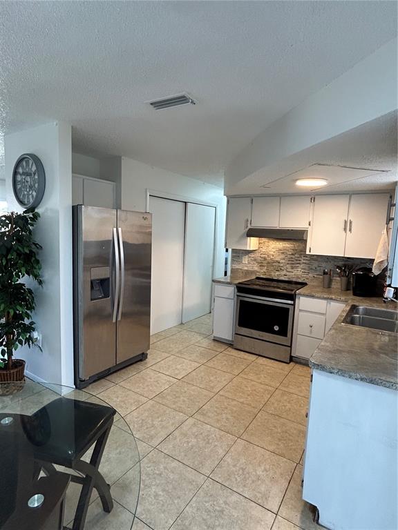 A kitchen features stainless steel appliances, white cabinets, and a tiled floor — 7808 OSTEEN ROAD, NEW PORT RICHEY, FL