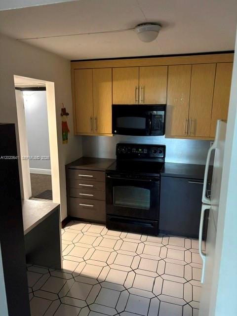 A kitchen features light wood upper cabinets, dark lower cabinets, black appliances, and patterned tile flooring — 2781 Taft St # 411, Hollywood FL 33020, HOLLYWOOD, FL