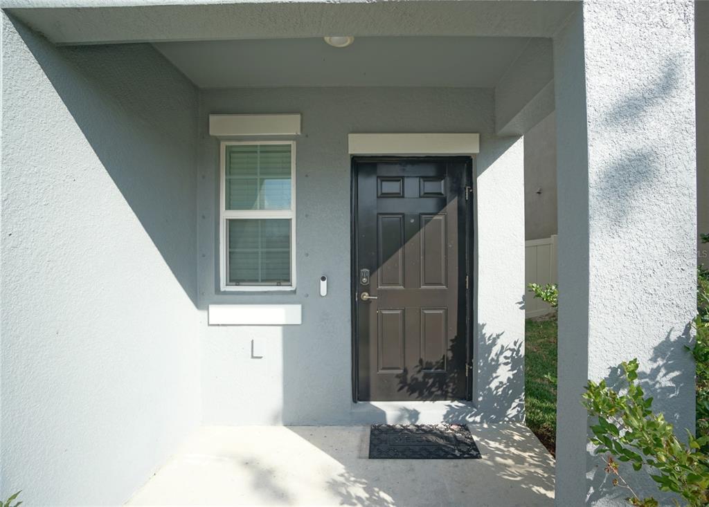 A covered entryway features a black front door, a single window, and a welcome mat — 9904 CALYPSO ORCHID COURT, RIVERVIEW, FL