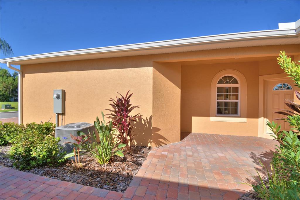 The exterior of a house features a tan stucco wall, a brick paver walkway, and landscaping — 1709 LINZ CT, WINTER HAVEN, FL