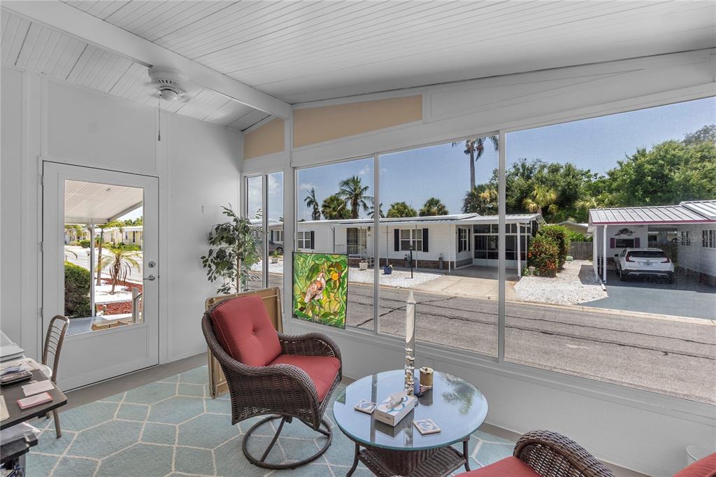 A sunroom with a wicker chair, glass table, and large windows overlooking a residential street — 45 CABALLO WAY, BRADENTON, FL