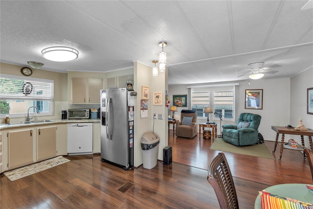 A kitchen with stainless steel appliances and wood-look flooring opens into a carpeted living area — 45 CABALLO WAY, BRADENTON, FL