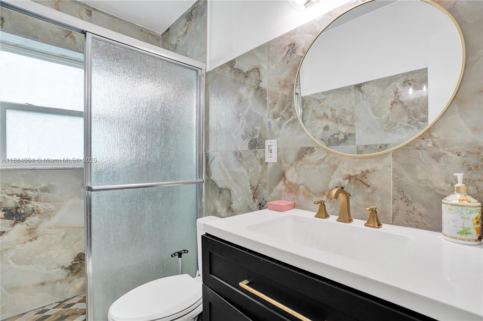 A bathroom features a black vanity, gold fixtures, a round mirror, and marble-patterned wall tiles — 320 N 71st Ave, Hollywood FL 33024, HOLLYWOOD, FL