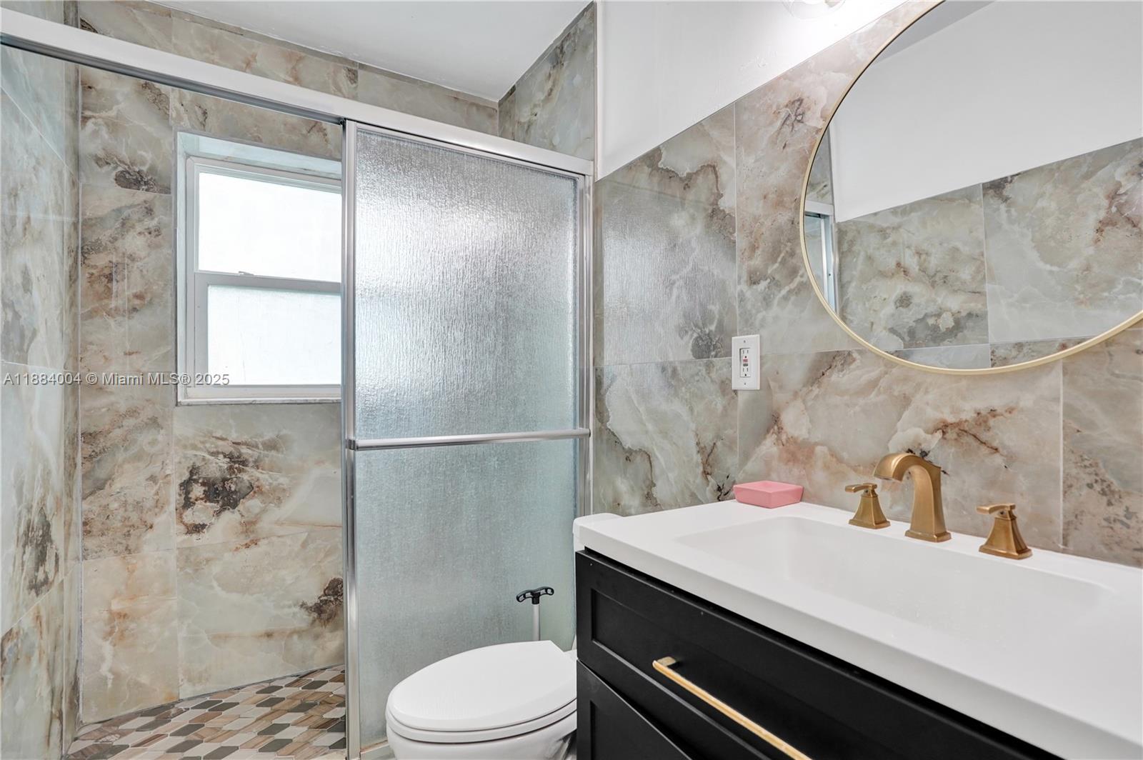 A bathroom features marble-patterned wall tiles, a black vanity, and a glass-enclosed shower — 320 N 71st Ave, Hollywood FL 33024, HOLLYWOOD, FL
